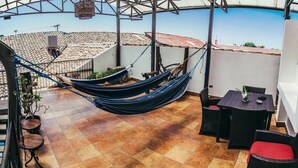 A hammock on a tiled patio with a pool in the background. - Hotel San Juan de León (León)