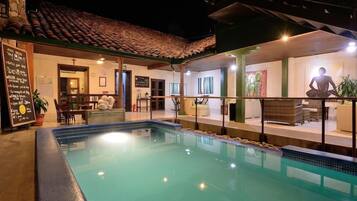 Zona de piscina con área de descanso cubierta y una estatua.