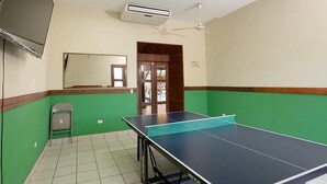 A room with a ping pong table, a ceiling fan, an air conditioning unit, a mirror, and a door leading to another room. - Hotel San Juan de León (León)