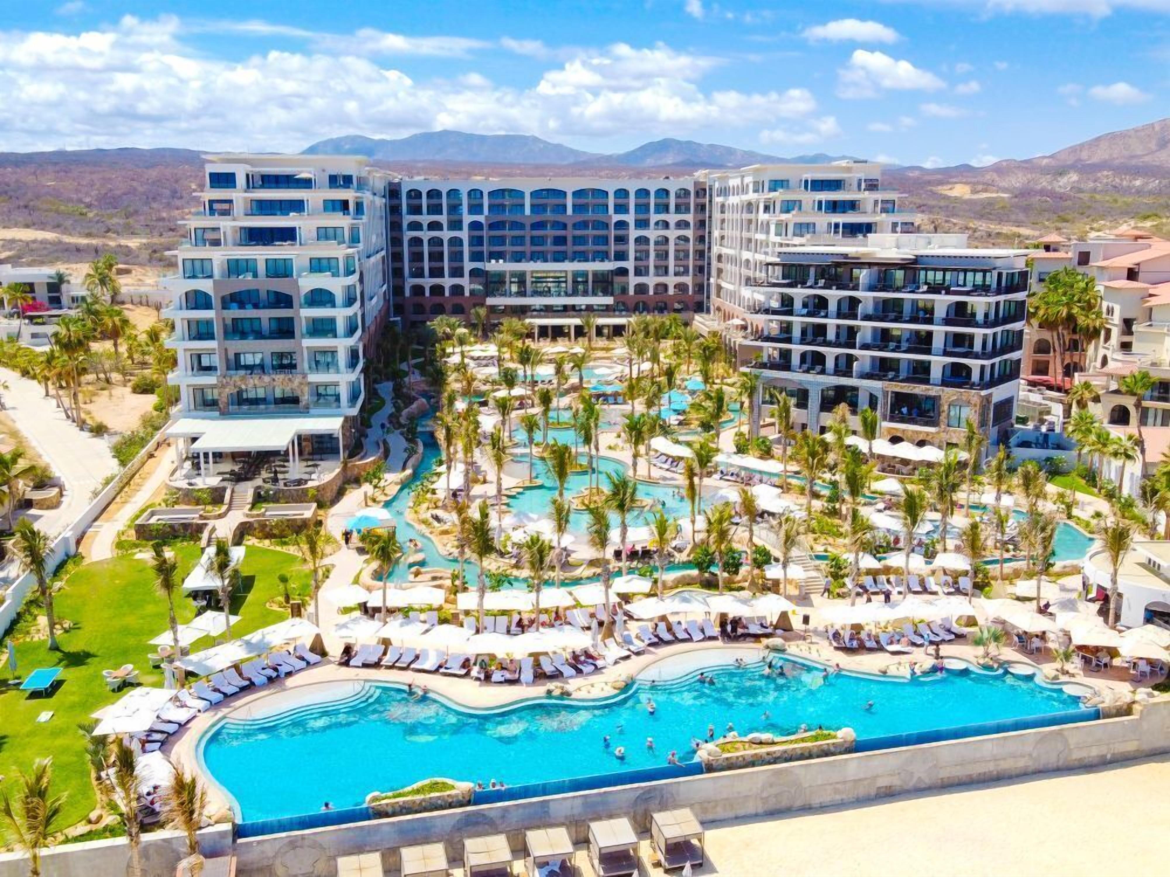 Un resort con varias piscinas, palmeras y edificios modernos.