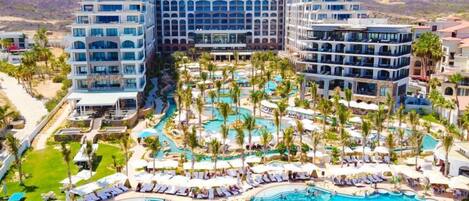 Un resort con varias piscinas, palmeras y edificios modernos.