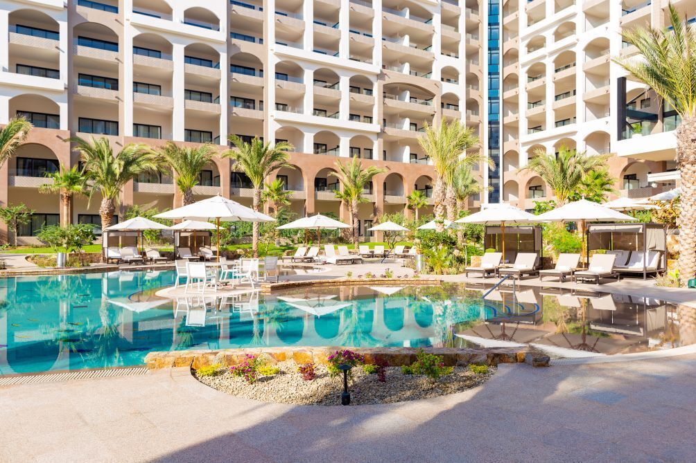 Zona de piscina d'hotel amb diversos nivells de balcons, gandules i ombrelles.