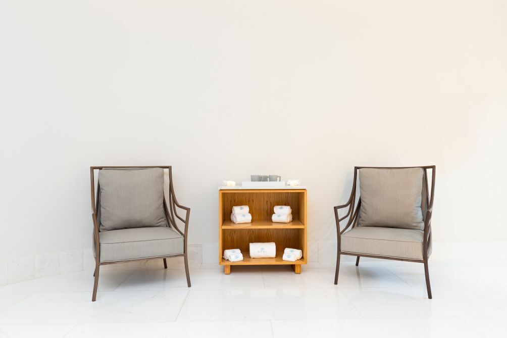 Two chairs with grey cushions and a wooden shelf with folded towels in between.