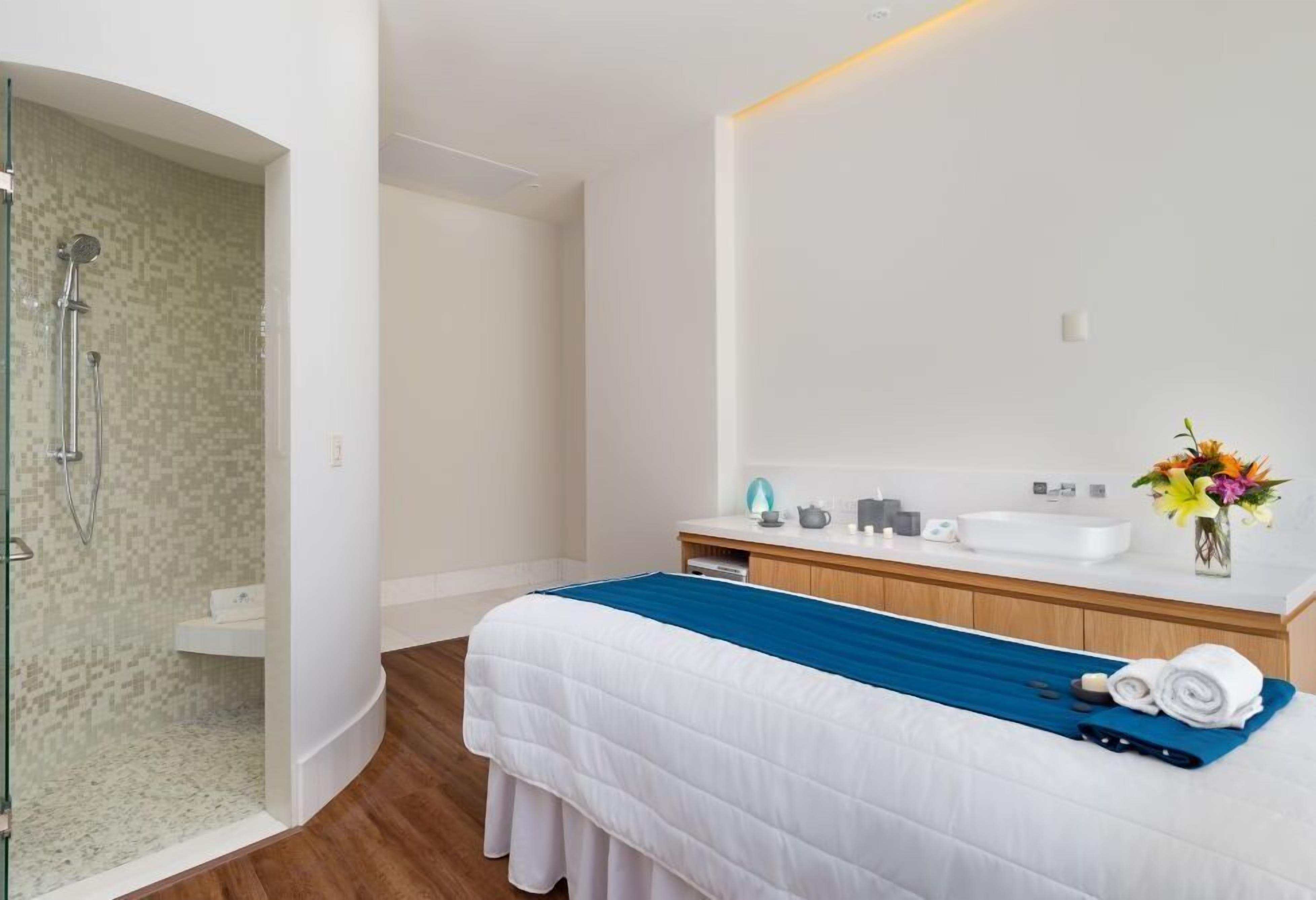 Una habitación de hotel moderna con cama, ducha, lavamanos y tocador.