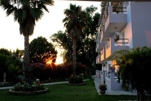 Hotel con jardín que presenta palmeras y plantas en flor, un sendero y un edificio con balcones.