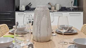 Et moderne køkken med mørke skabe, en marmorbeklædt bagvæg og et spiseområde med hvide tallerkener, skåle og glas.