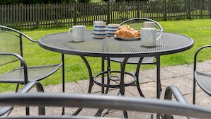 Une table ronde en métal, des chaises, un croissant et deux tasses.