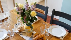 Une table à manger dressée avec des assiettes, des verres, un vase de fleurs et du pain.