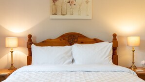 Un lit bien fait, avec une tête de lit en bois, deux lampes de chevet et un tableau représentant des vases accroché au mur.