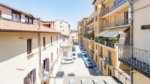 Una stretta via costeggiata da edifici a più piani con balconi, auto parcheggiate e un cielo sereno.