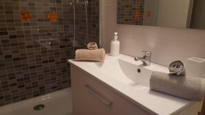 Une salle de bain avec un lavabo blanc, un miroir, une douche avec une porte en verre et deux serviettes posées sur le lavabo.