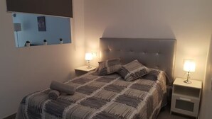 Un lit bien fait, recouvert d’une couvre-lit à motifs, avec deux lampes de chevet et un miroir accroché au mur.