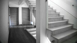 Una escalera moderna con barandilla de vidrio, que conduce a una plataforma con dos puertas cerradas.