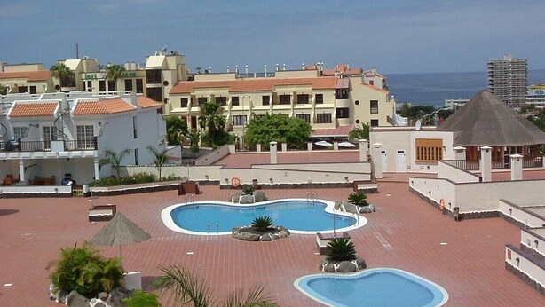 A rooftop pool area with two swimming pools, surrounded by buildings and a view of the ocean. - El Mirador (Los Cristianos)