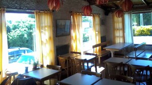 A restaurant interior with wooden tables and chairs, large windows with curtains, and hanging decorations. - Residencia Familiar La Rosa (San Carlos de Bariloche)