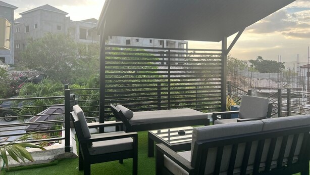 Een dakterras met buitenmeubilair, een pergola en uitzicht op omliggende gebouwen en groen.