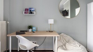 Une chambre à coucher avec un lit, un bureau avec une chaise, un miroir rond et une étagère remplie de livres.