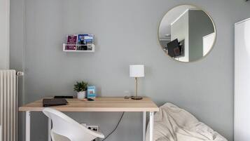 Un dormitorio con una cama, un escritorio con una silla, un espejo redondo y una estantería con libros.