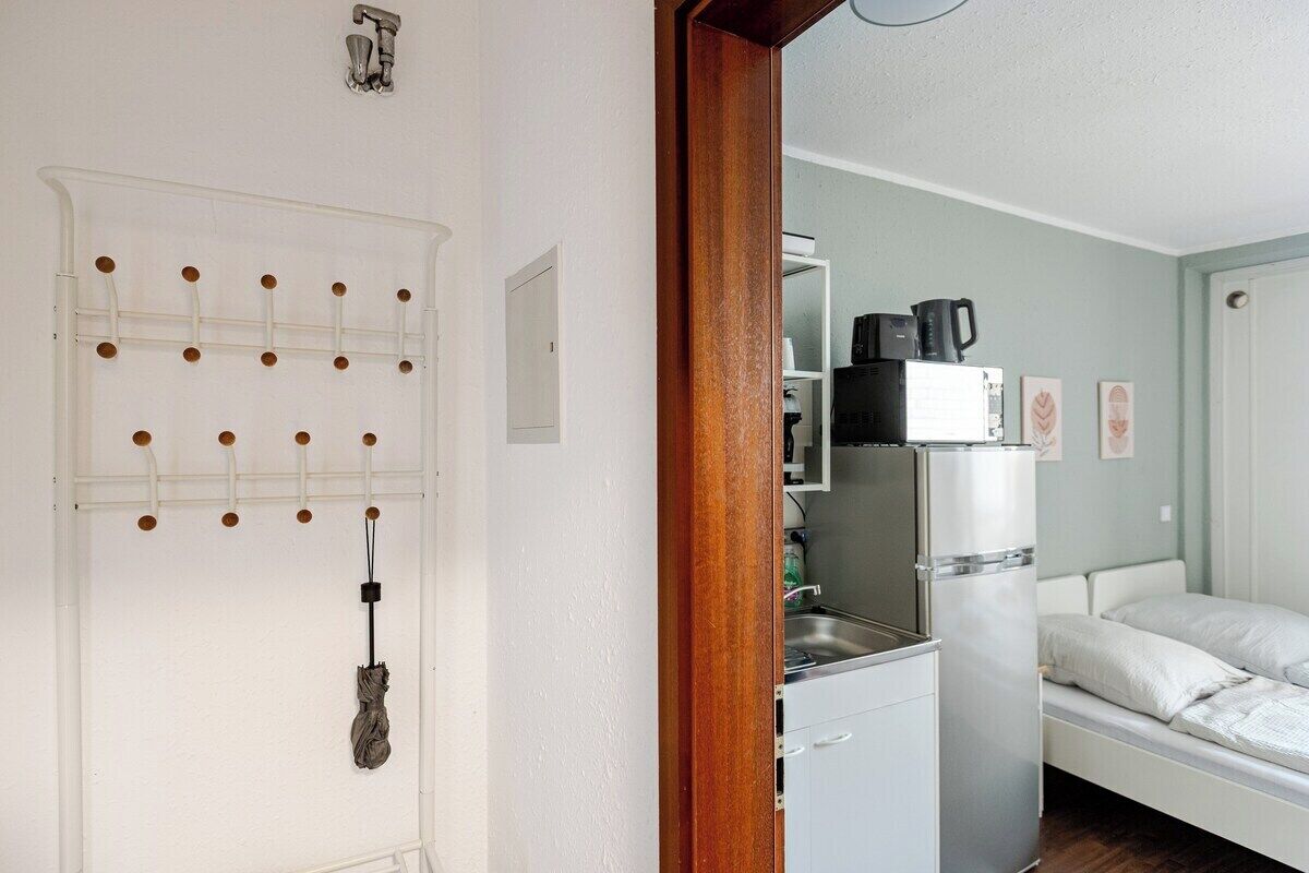 Una habitación pequeña con cama, kitchenette y una puerta con un tablero perforado.