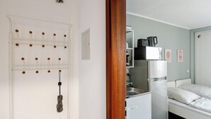 Une petite pièce comprenant un lit, un coin cuisine et une porte dotée d’un panneau perforé.