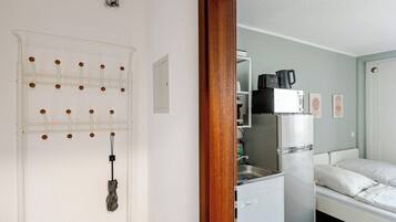 Una habitación pequeña con cama, kitchenette y una puerta con un tablero perforado.