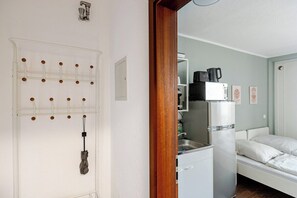 A compact room with a bed, a kitchenette, and a door with a pegboard.