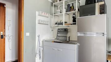 Una cocina compacta con microondas integrado, refrigerador y una pequeña encimera.