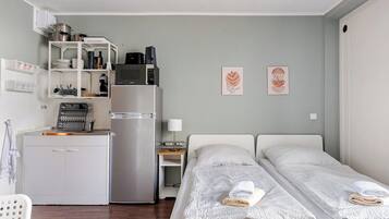 A compact room with a kitchenette, two beds, and a small table with a lamp.