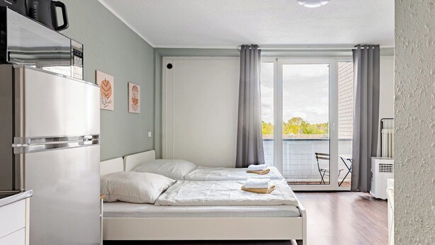 A modern bedroom with a bed, a built-in refrigerator, and a sliding glass door to a balcony. - Exklusiv | Küche | Office | Streaming+Minibar 6311 (Bonn)