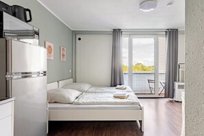 A modern bedroom with a bed, a built-in refrigerator, and a sliding glass door to a balcony.
