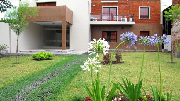Et moderne hus med fladt tag, balkon og en velplejet græsplæne med blomster.