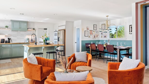 A modern kitchen with a dining area, featuring orange chairs and a chandelier.
