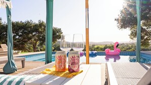 A poolside table with two bottles of Cavi Squeeza Peach and Raspberry Lime, a pink flamingo float, and lounge chairs with a view of the pool and landscape.