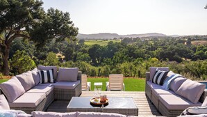 An outdoor seating area with wicker furniture and a glass table, overlooking a lush landscape.