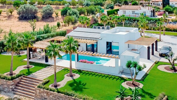 A modern house with a swimming pool, surrounded by palm trees and a well-maintained lawn.