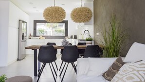 A modern kitchen with a dining area, featuring a large window, two hanging light fixtures, and a dining table with chairs.