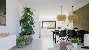 A modern kitchen with white cabinets, a dining area with black chairs, and large potted plants.