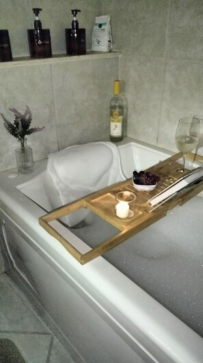 A bathroom with a bathtub, a wooden tray with a candle, a glass of wine, and a bottle of lotion.