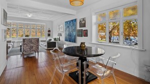 A spacious room with a round table, clear chairs, a sofa, and a large window with autumn foliage. - Lakeside Retreat - Cromwell Holiday Home (Cromwell)