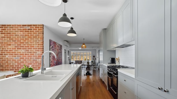 A modern kitchen with white cabinetry, a brick accent wall, and a central island with a sink. - Lakeside Retreat - Cromwell Holiday Home (Cromwell)