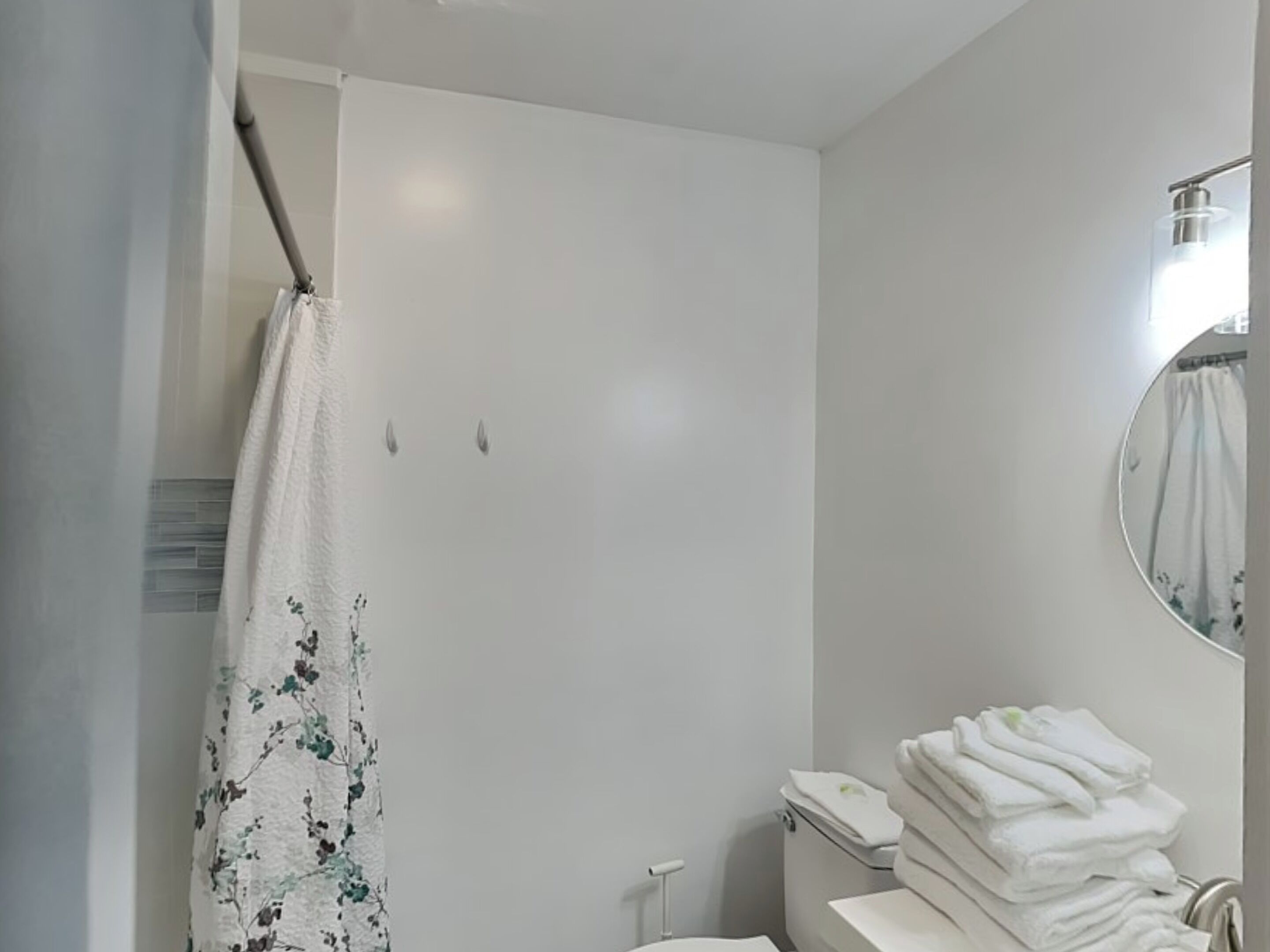 A bathroom with a shower, toilet, and a stack of towels.
