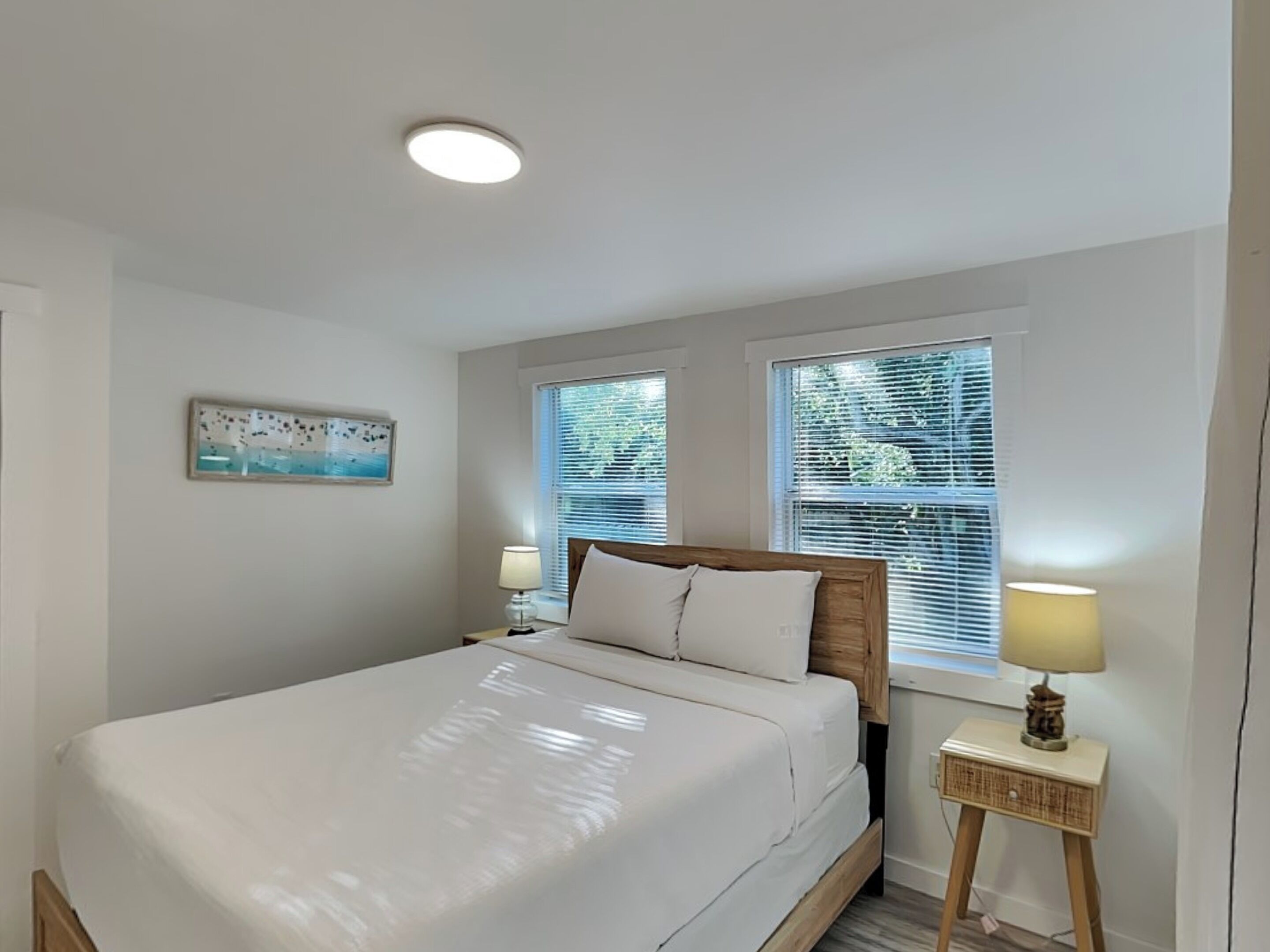 A bedroom with a bed, two bedside tables with lamps, a ceiling light, and a window with blinds.