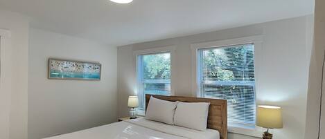 A bedroom with a bed, two bedside tables with lamps, a ceiling light, and a window with blinds.