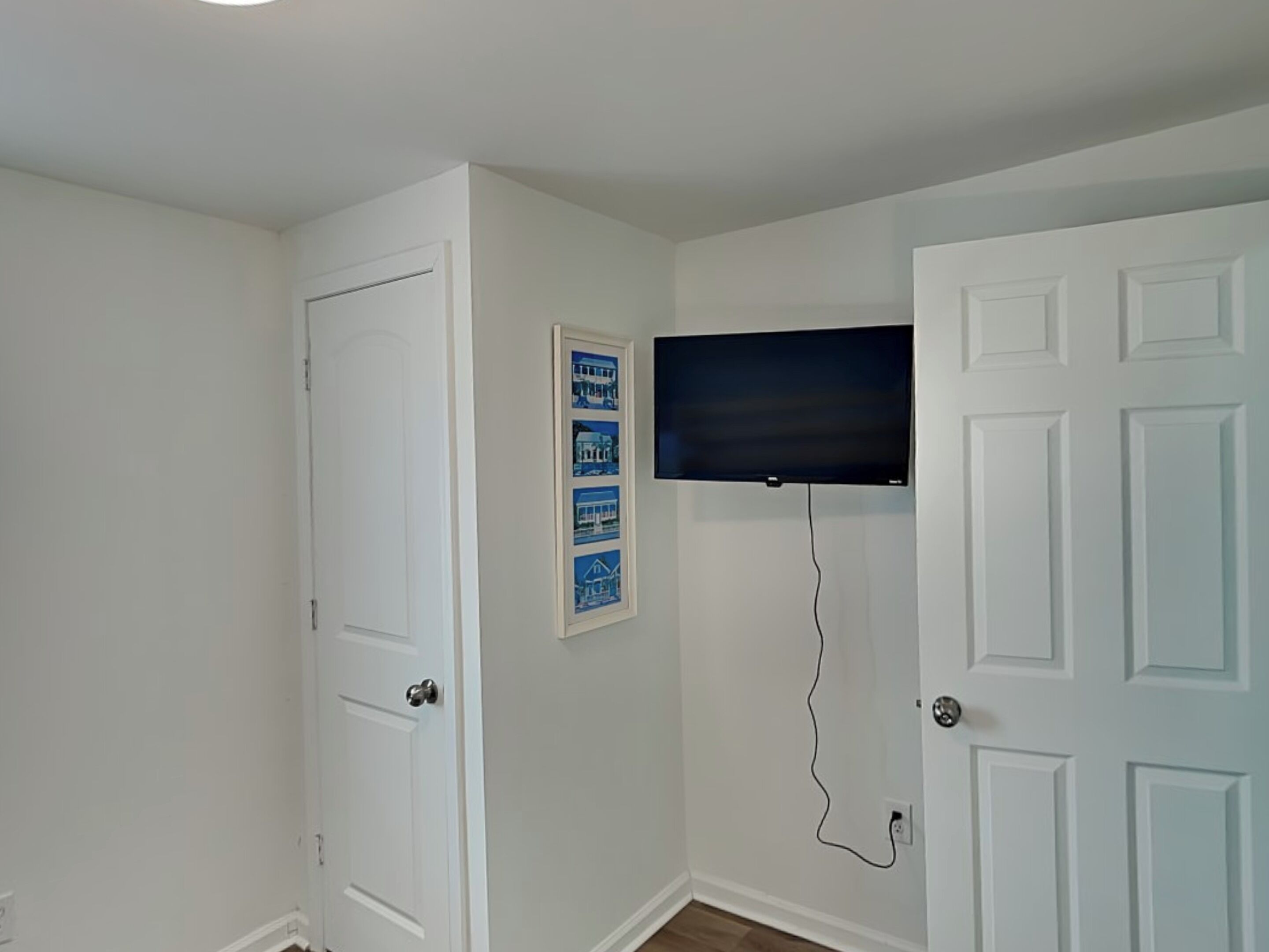 A room with white walls, a door, a framed picture, and a mounted TV.
