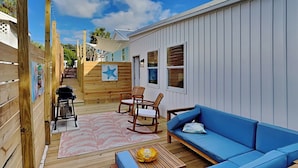 A wooden deck with a blue sofa, rocking chairs, and a grill. - Salt & Sea by Resort Collection (Panama City Beach)