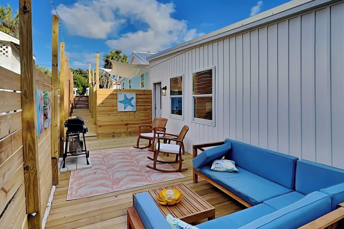 A wooden deck with a blue sofa, rocking chairs, and a grill.