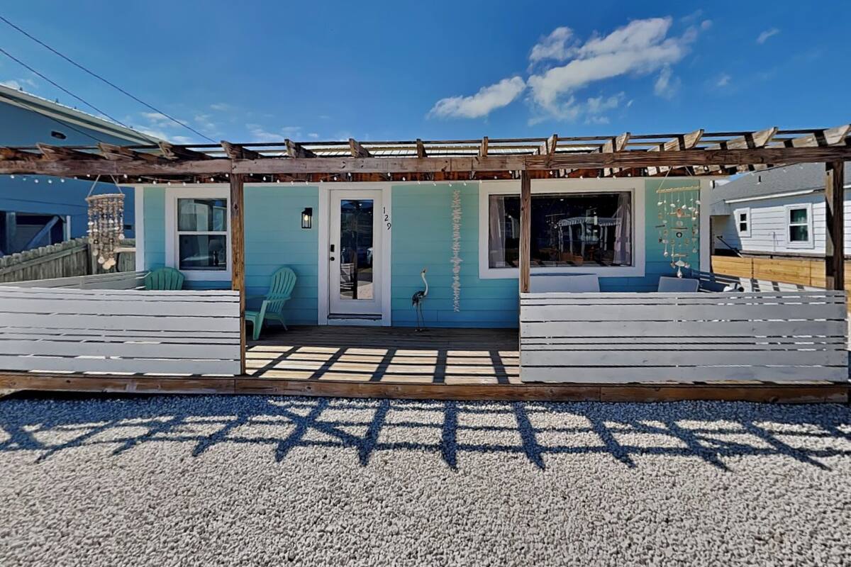 A coastal building with a wooden deck, a turquoise facade, and a clear sky.