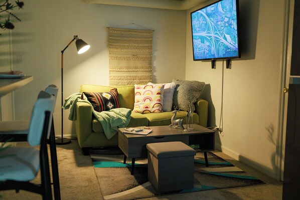 Una sala de estar con un sofá verde, una mesa de centro, una lámpara y un televisor montado en la pared.
