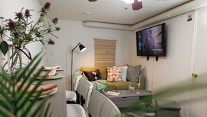 Ein modernes Wohnzimmer mit einer Couch, Sesseln, einem Couchtisch, einem Fernseher und einer Pflanze.