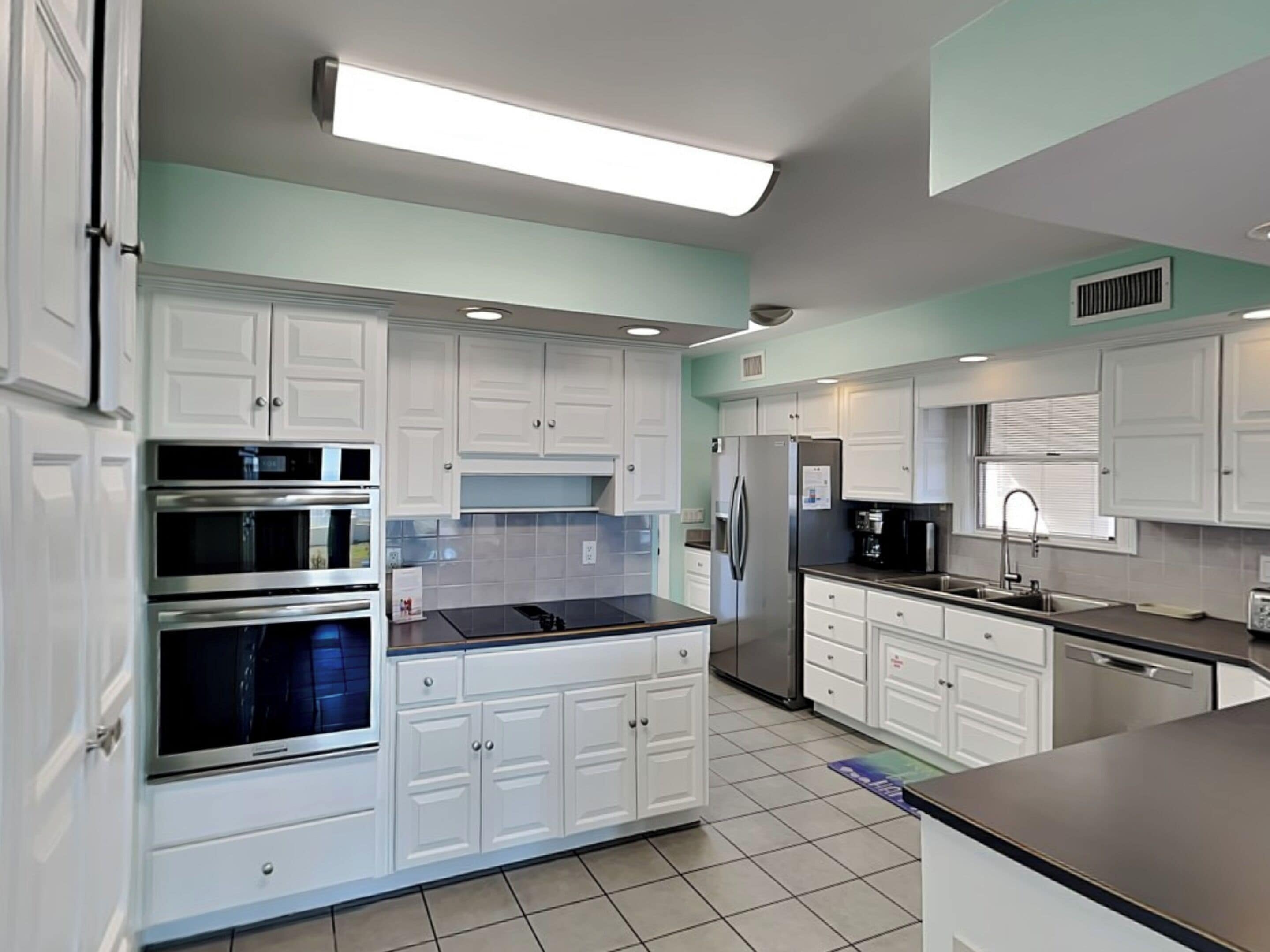 Una cocina moderna con armarios blancos, electrodomésticos de acero inoxidable y piso de baldosas.